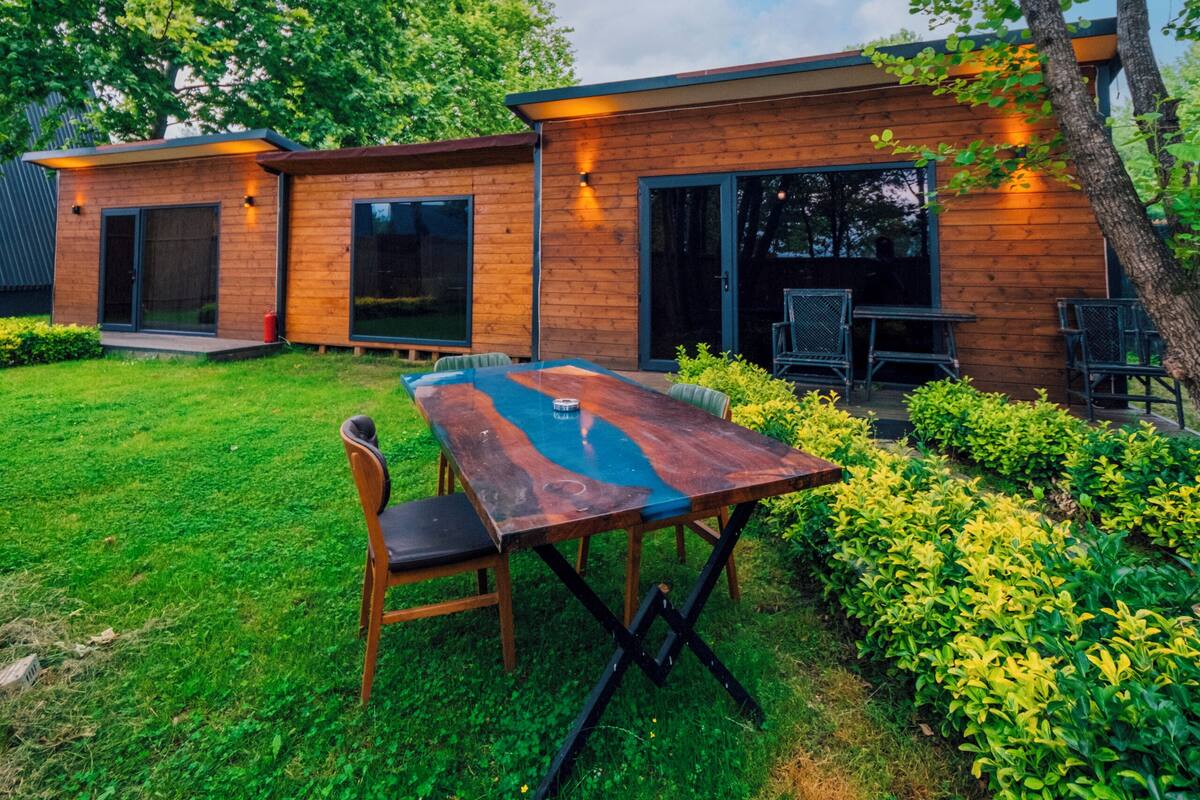 A modern house with a wooden exterior, a dining table with chairs, and a well-maintained garden.