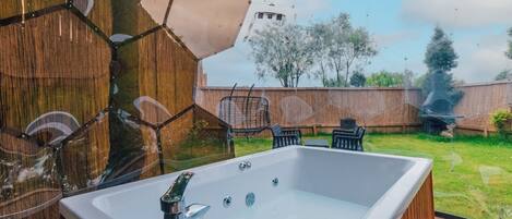 Un jacuzzi en una terraza de madera con vista a un jardín trasero.