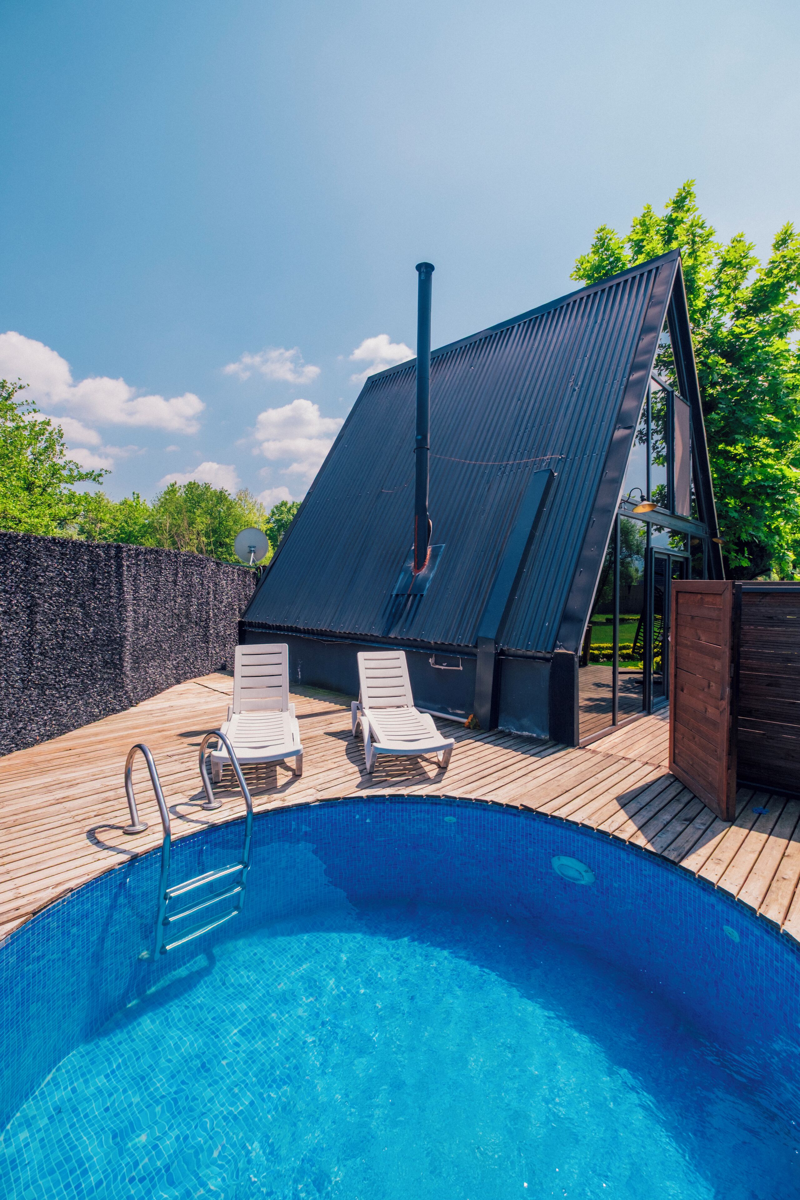 A swimming pool with two lounge chairs and a covered area with a metal roof.