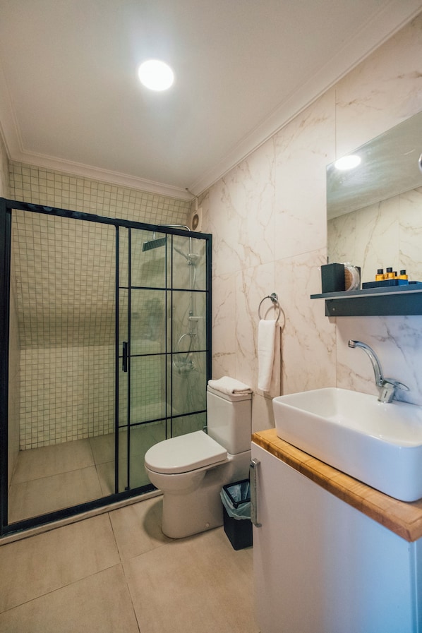 Une salle de bain moderne avec une douche à parois de verre, des toilettes blanches et un lavabo doté d’un plan de travail en bois.
