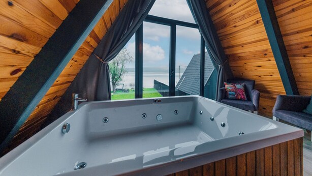 Un baño moderno con una bañera grande, techo de madera y vistas a un paisaje verde.