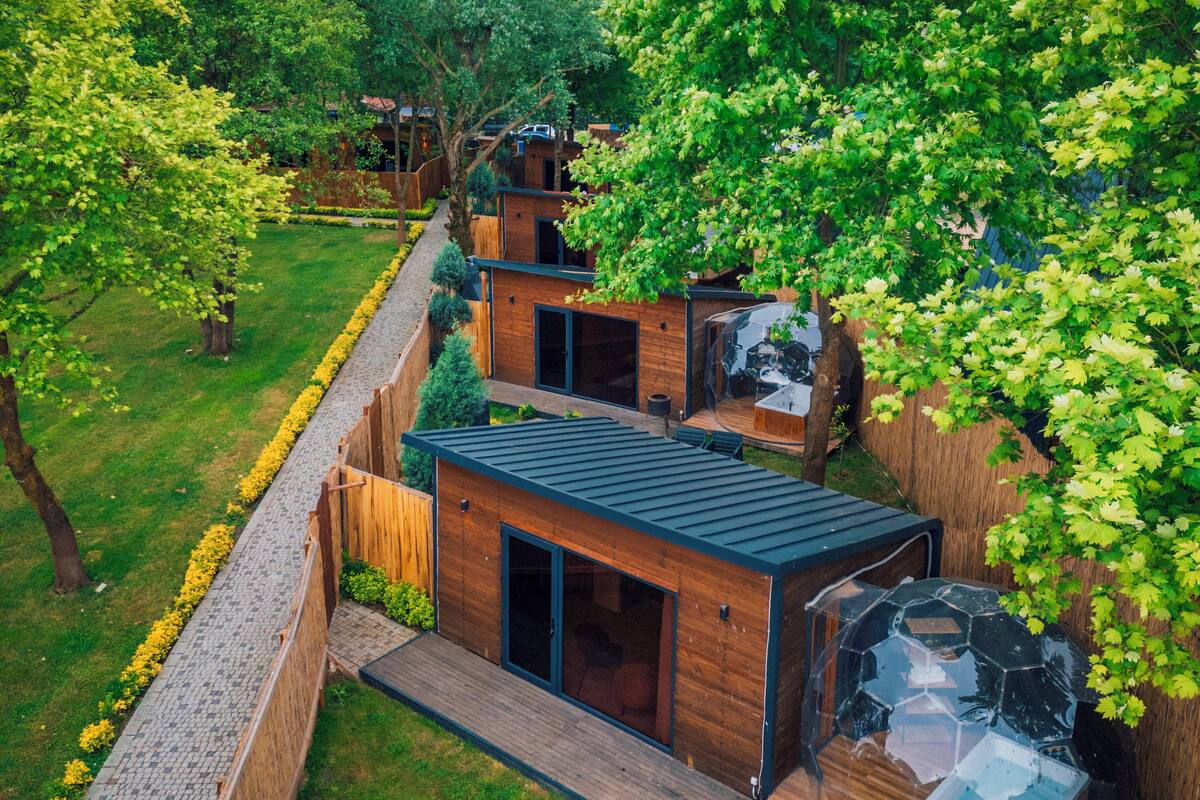 A modern outdoor living area with wooden structures, a hot tub, and a view of a lush garden.