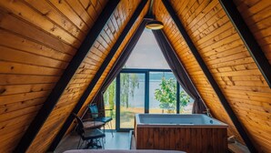 Un dormitorio en ático con techo de madera inclinado, una cama grande, una mesita pequeña y vistas al exterior.