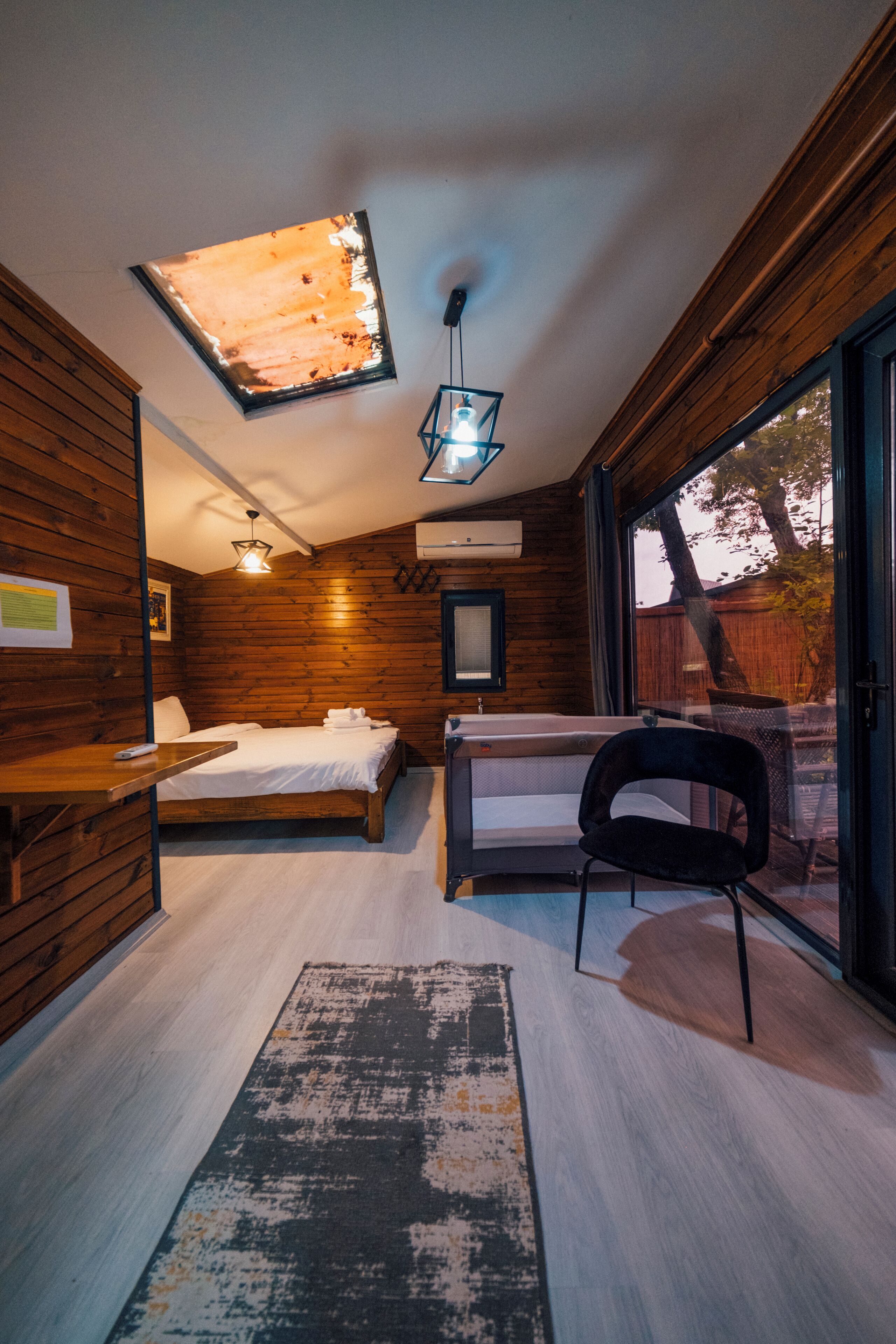 A modern bedroom with a wooden interior, a large window, a bed, a desk, and a chair.