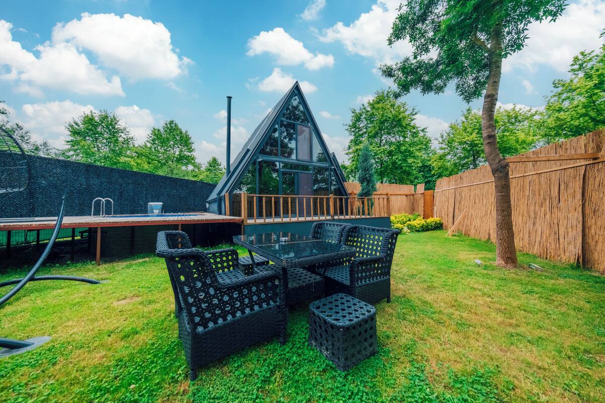A modern house with a triangular roof, a glass conservatory, and a patio with wicker furniture.