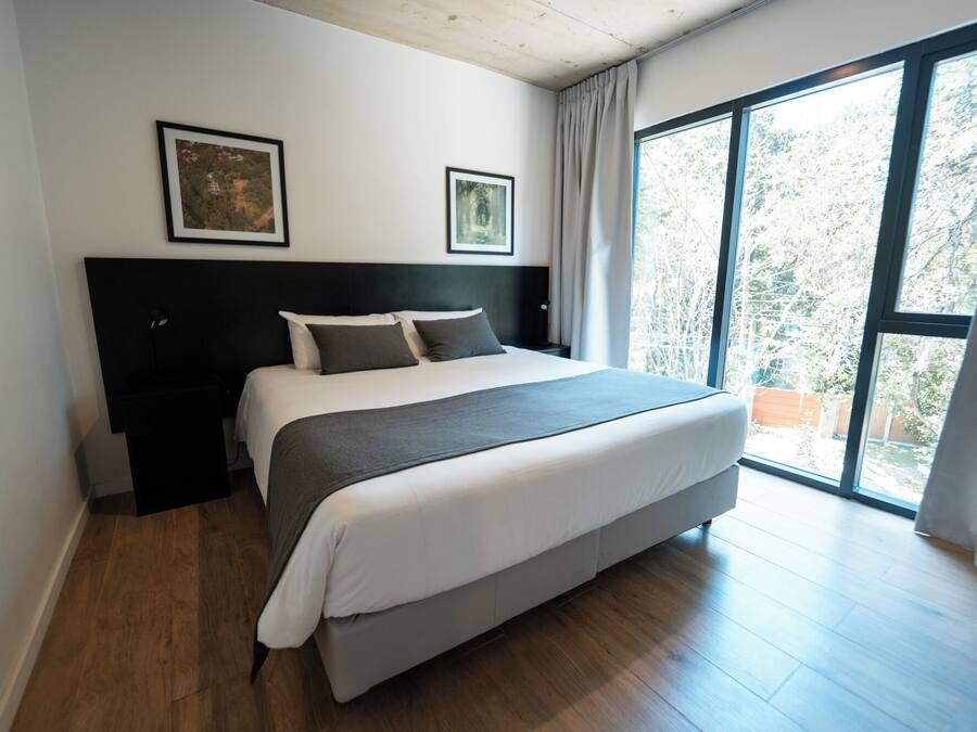 Um quarto moderno com uma cama grande, uma cabeceira escura e duas fotos emolduradas na parede.
