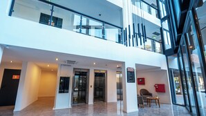 A modern hotel lobby with a glass elevator, a reception desk, and a seating area. - Mérit Parque Leloir by Amérian (Villa Udaondo)