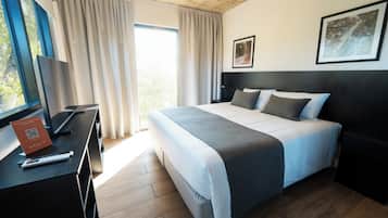Habitación de hotel moderna con una cama grande, un escritorio con una computadora portátil, una ventana con cortinas y un cuadro en la pared.