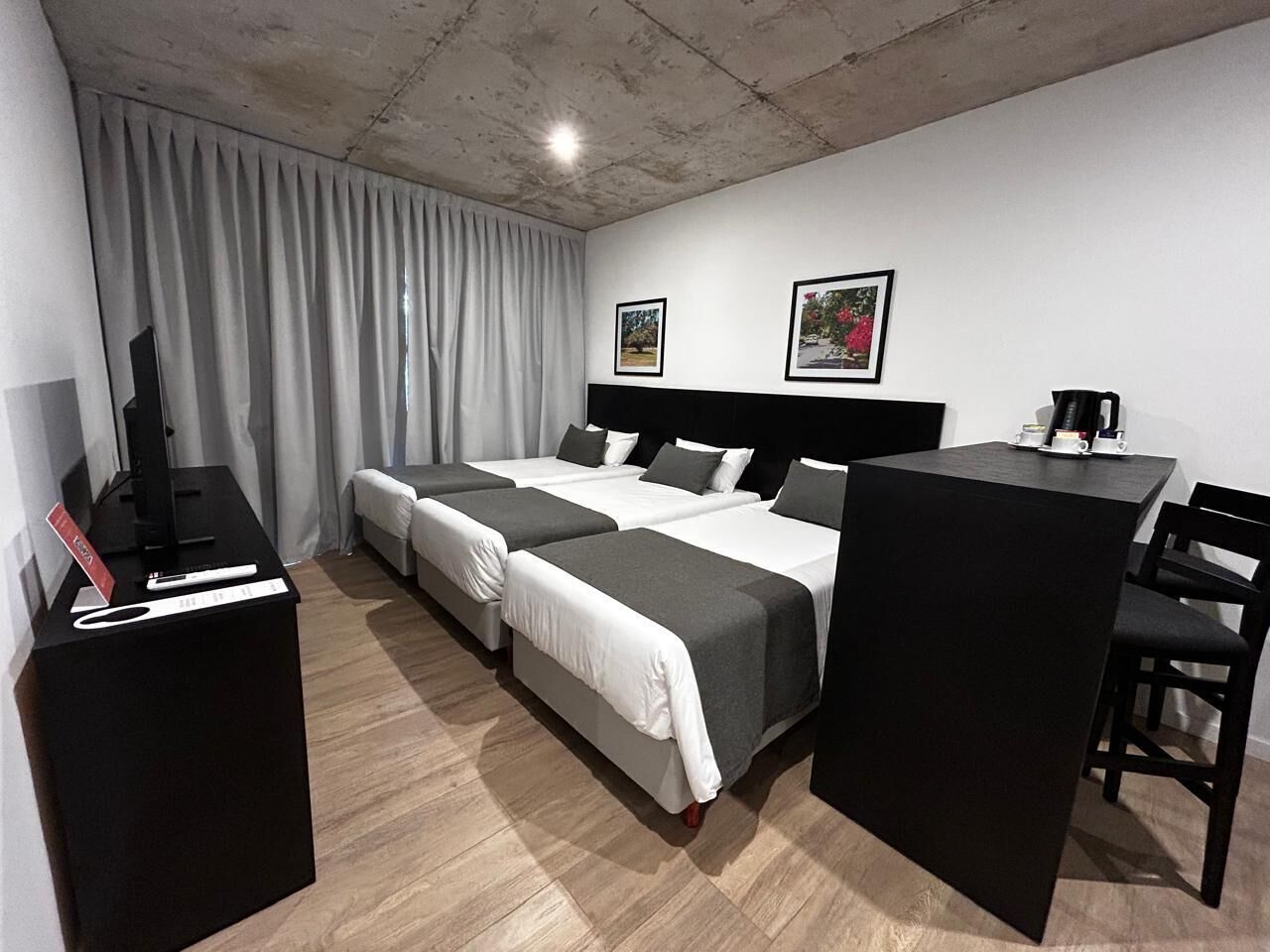 Habitación de hotel con dos camas individuales, un escritorio, una silla, un televisor y un perchero.