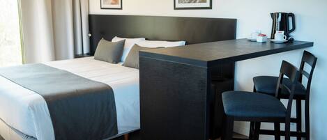Una habitación de hotel moderna con una cama, un escritorio con una silla y dos cuadros en la pared.