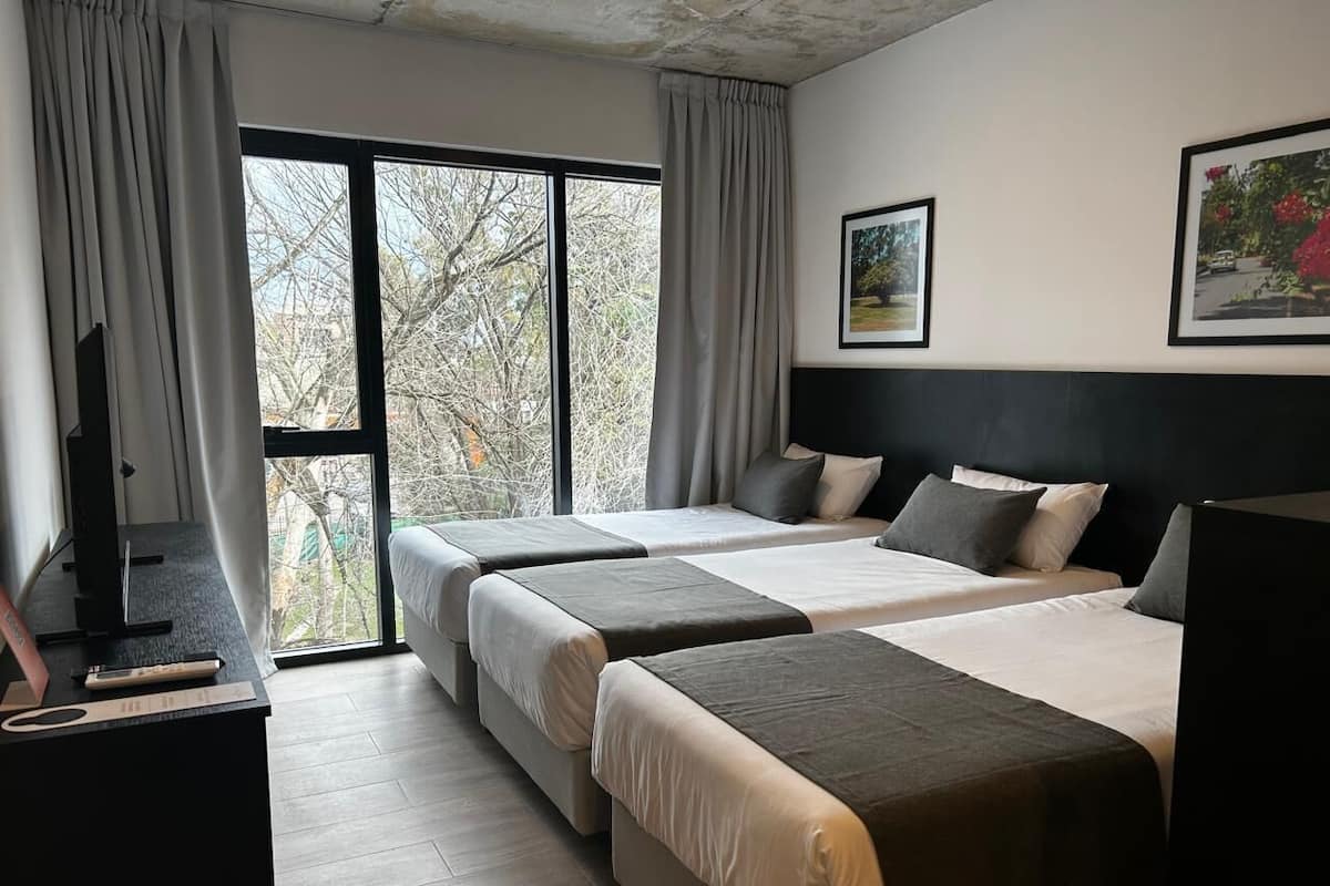 A hotel room with two beds, a desk with a computer, and a large window with curtains.