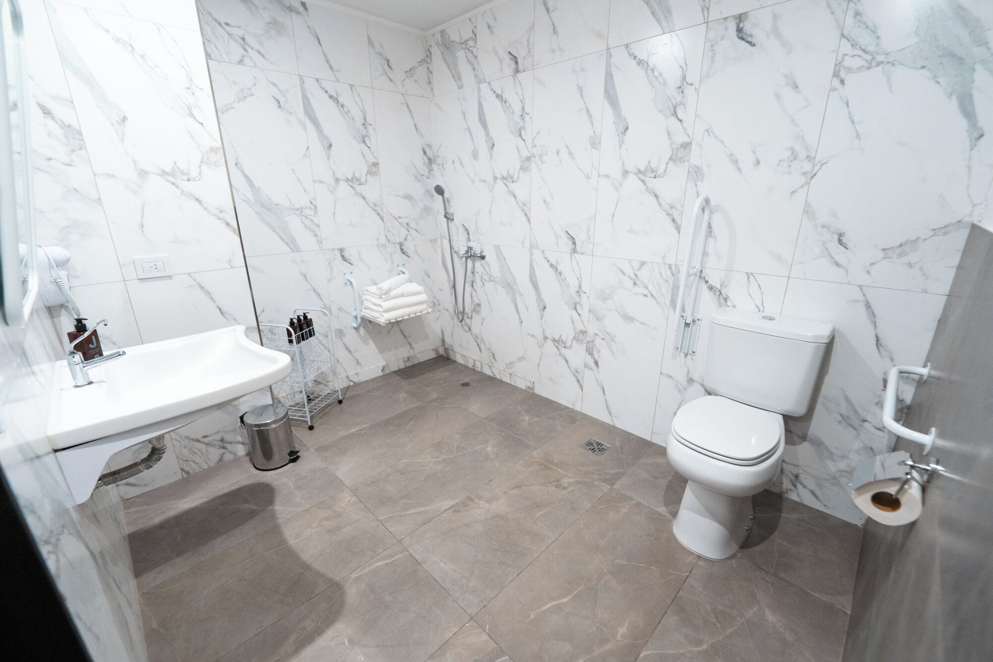 Une salle de bain avec un lavabo blanc, des toilettes et des murs en marbre.