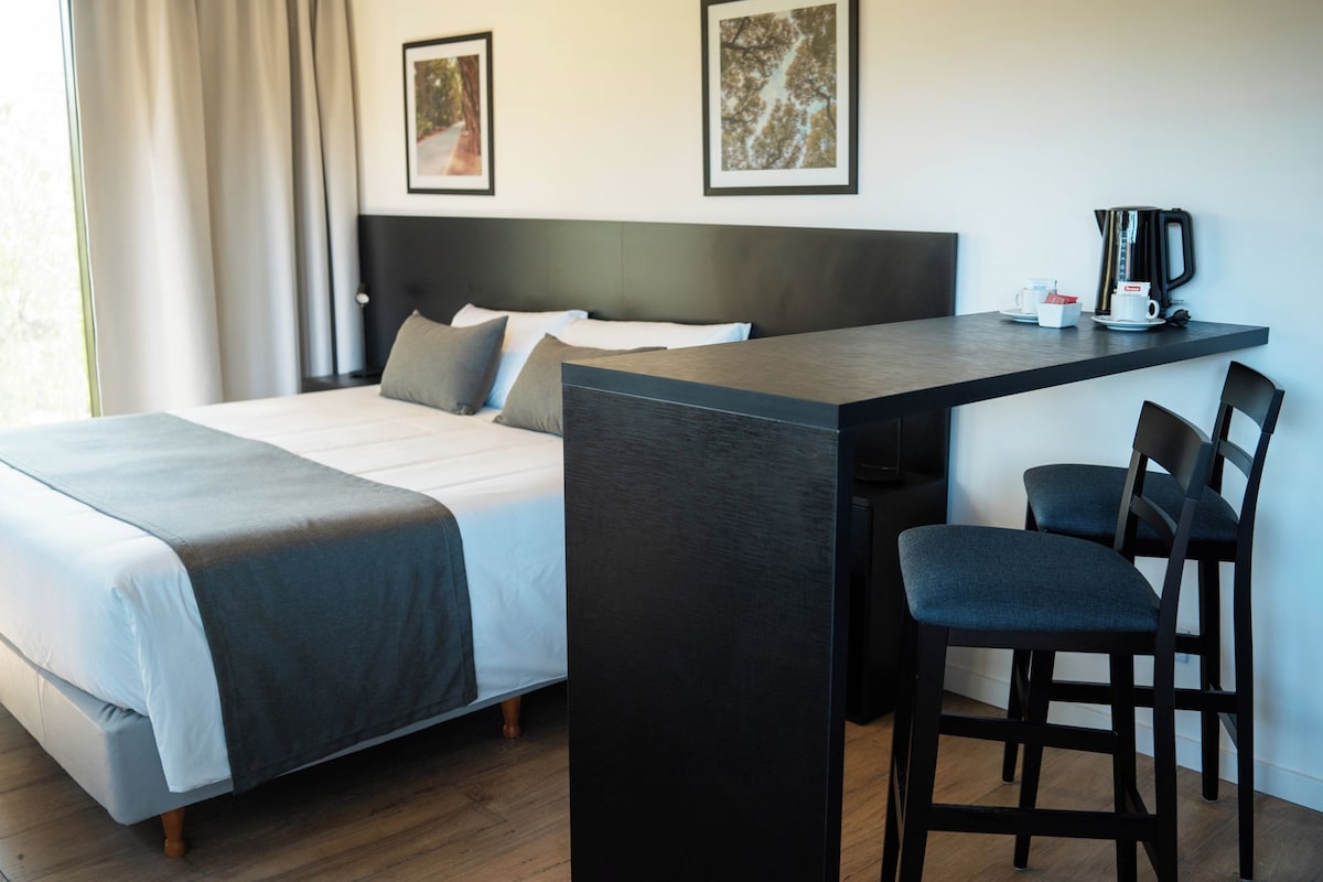 A modern hotel room with a bed, a desk with a chair, and two framed pictures on the wall.