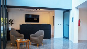 A reception area with two armchairs, a small table with a plant, and a flat-screen TV mounted on the wall. - Mérit Parque Leloir by Amérian (Villa Udaondo)