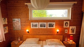 A wooden cabin bedroom with two beds, a nightstand with a lamp, and framed photos on the wall.