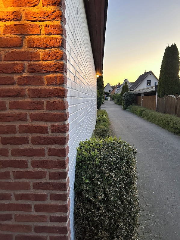 Una pared de ladrillo con adornos blancos y un seto a lo largo de una calle residencial.