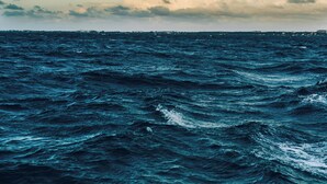 Vista do oceano, com ondas e uma linha de costa distante.