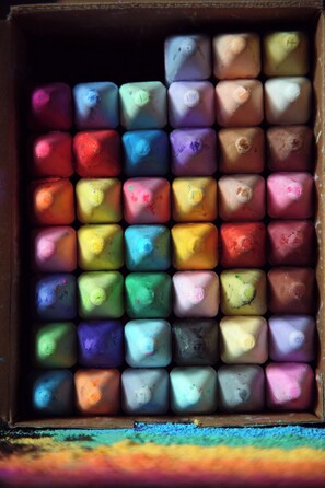 Chalks are arranged in a grid pattern within a wooden box.