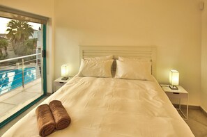 Quarto de hotel com uma cama grande, duas luminárias de cabeceira e vista para uma piscina.