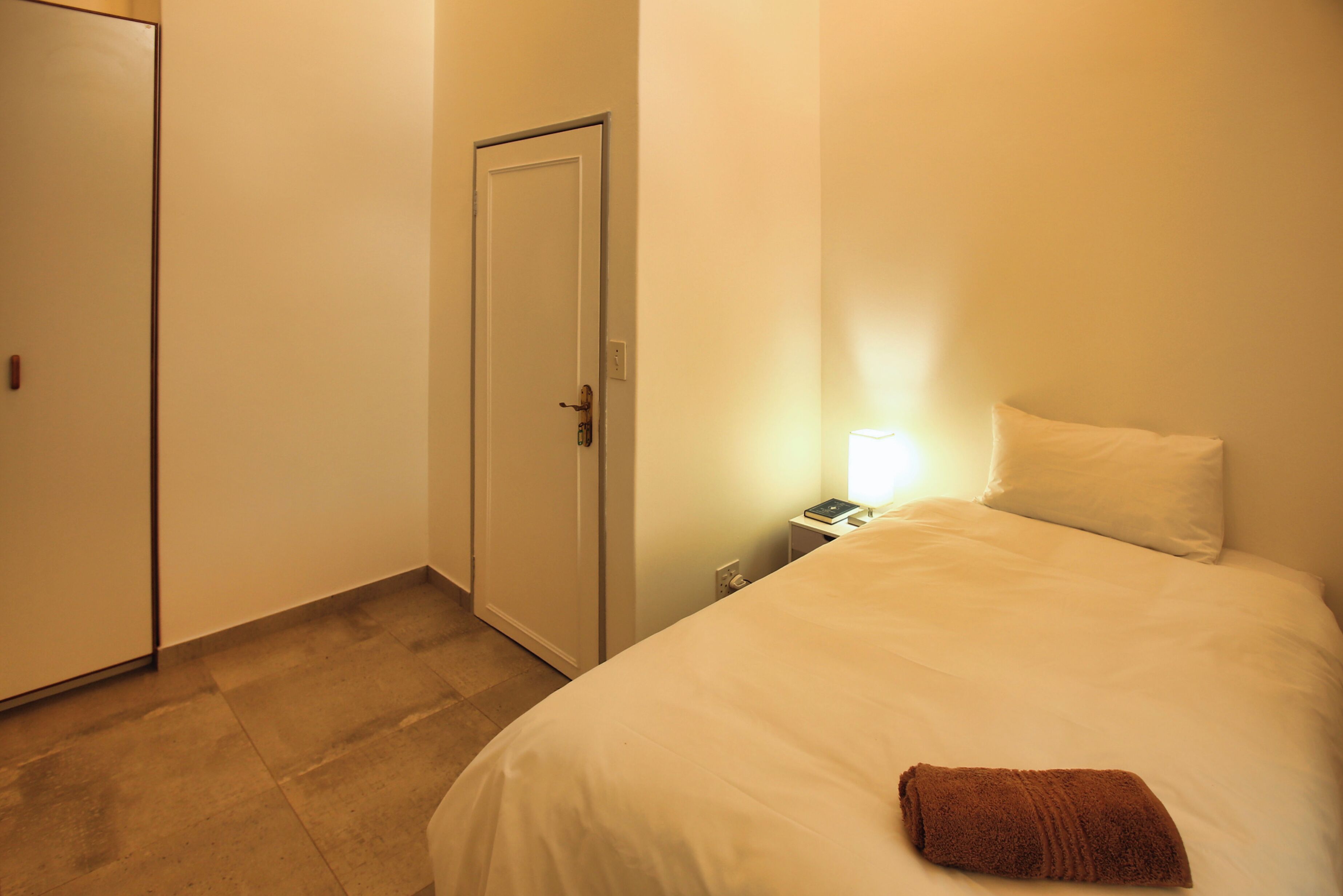 Una habitación de hotel con una cama, una mesita de noche, una lámpara y una puerta.