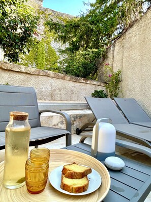 Un espacio al aire libre con una mesa preparada para dos, que incluye una botella, vasos y pan.