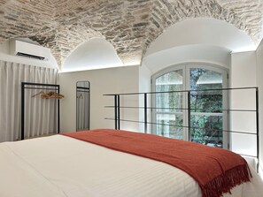 Un dormitorio con una cama grande, una manta roja, un armario, un espejo y una ventana con vistas a zonas verdes.