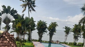 Une piscine dont le bord est orné d’un motif à carreaux, entourée de palmiers et offrant une vue sur la mer.