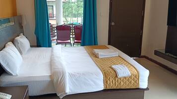 Quarto de hotel com cama, televisão, escrivaninha com telefone e vista para área externa com cadeiras e mesa.