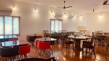 Un comedor con mesas y sillas redondas, unidades de aire acondicionado y ventiladores de techo.