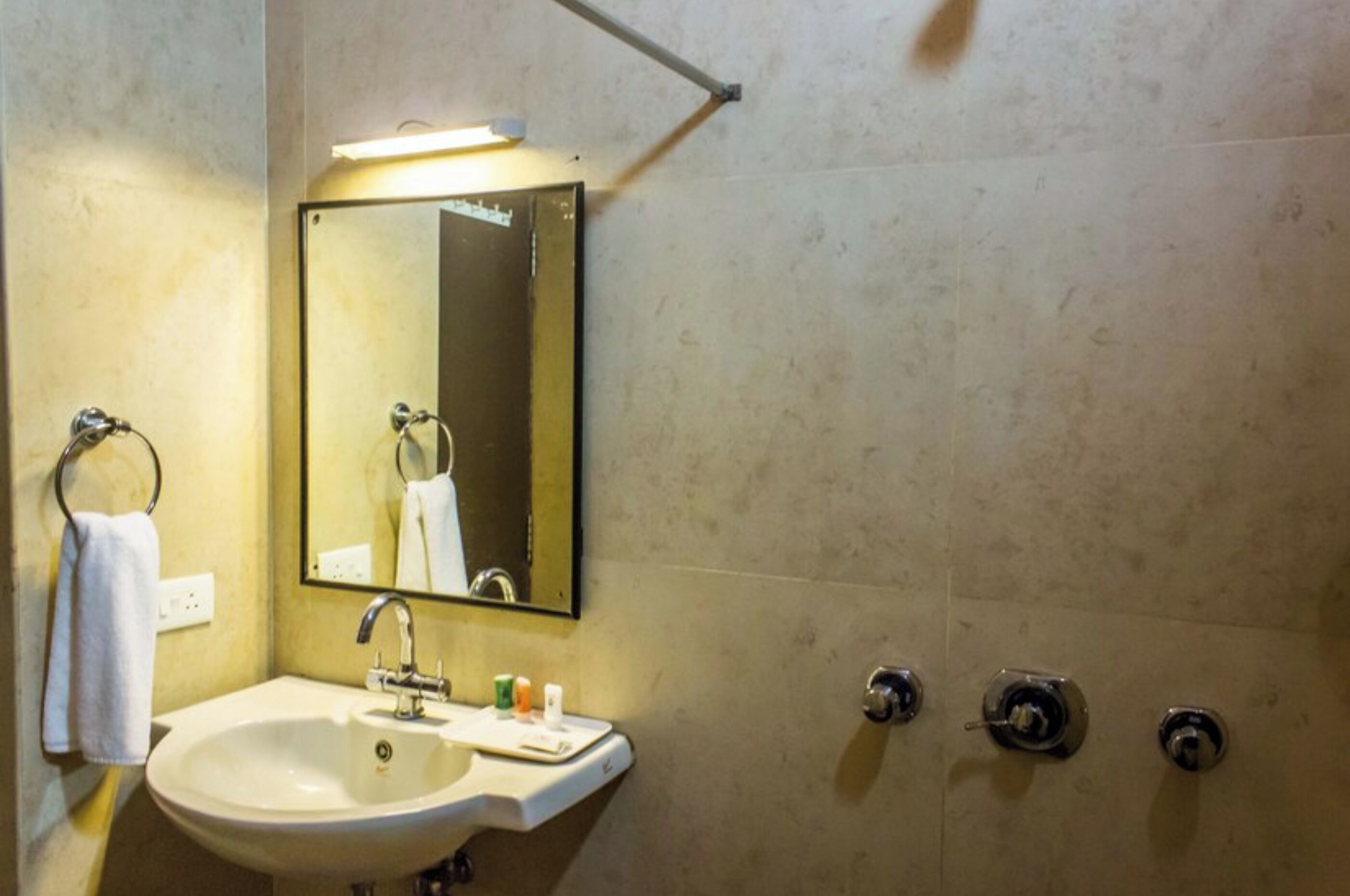 A bathroom with a sink, mirror, towel rack, and two towel dispensers.