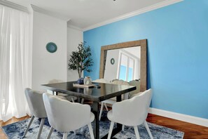 Un coin repas avec une table en bois foncé, des chaises blanches et un mur d’accent bleu.