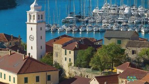 A marina with numerous boats docked, a white tower with a clock, and buildings with red-tiled roofs. - Luxury Villa Meden Dol with heated pool, Hot-Tub, 2 Saunas (Skradin)