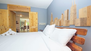 A bedroom with a wooden bed, white bedding, and a cityscape wall art. - Riverfront Luxury w/ Fire Pit & Chef's Kitchen (Bolingbrook)