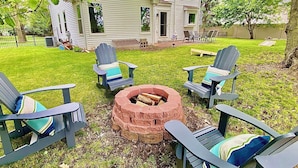 A backyard with a fire pit, four Adirondack chairs, and a house in the background. - Riverfront Luxury w/ Fire Pit & Chef's Kitchen (Bolingbrook)
