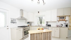 A modern kitchen with white cabinets, a wooden island, stainless steel appliances, and a coffee bar. - Riverfront Luxury w/ Fire Pit & Chef's Kitchen (Bolingbrook)