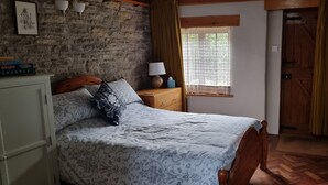 Een slaapkamer met een bed, een houten dressoir, een lamp en een raam met gordijnen.