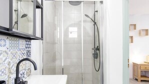 A modern bathroom with a glass-enclosed shower, a white sink, and a tiled backsplash.