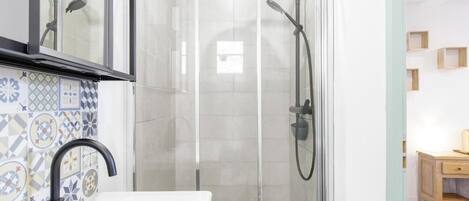 A modern bathroom with a glass-enclosed shower, a white sink, and a tiled backsplash.