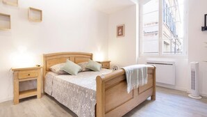 A bedroom with a wooden bed, bedside tables, a radiator, and a window with a view of buildings.