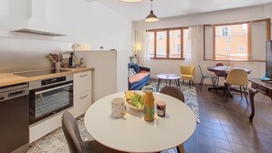Une cuisine moderne avec un coin repas, une grande fenêtre donnant sur les immeubles et un luminaire au plafond.
