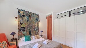 Une chambre à coucher avec un grand lit, une chaise, une armoire et une tapisserie murale.
