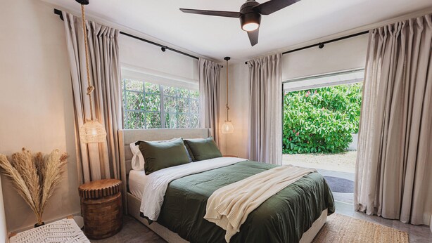 Une chambre à coucher avec un lit, une table de chevet, une lampe et une vue sur la verdure à l’extérieur.