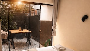 Habitación de hotel con cama, mesa y una silla frente a la puerta corrediza de vidrio.