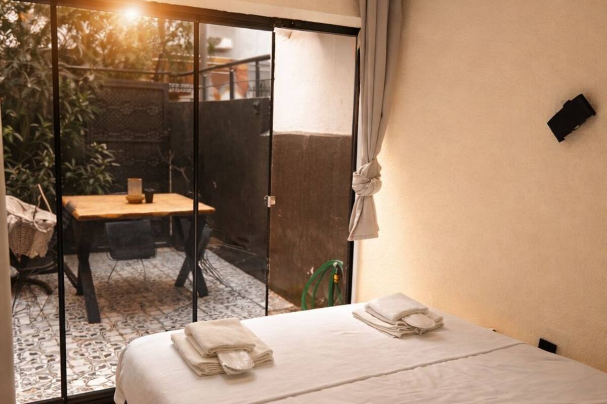 Habitación de hotel con cama, mesa y una silla frente a la puerta corrediza de vidrio.