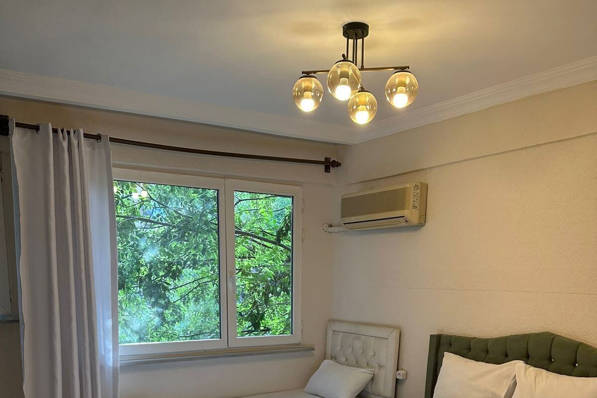 Habitación de hotel con dos camas, un ventanal con cortinas, una lámpara en el techo y un equipo de aire acondicionado.