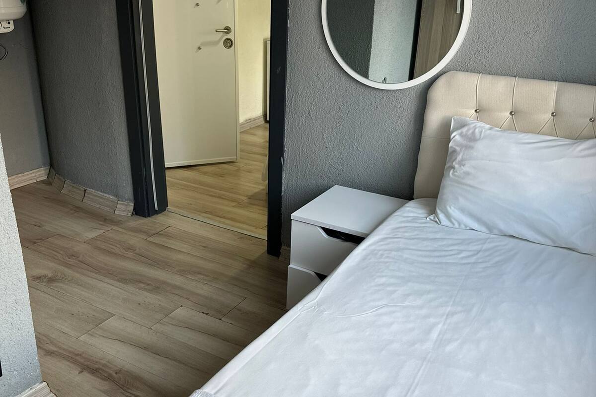 Un dormitorio con cama, mesita de noche, espejo y puerta que da a otra habitación.