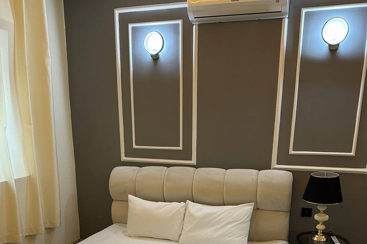 Una cama bien hecha con sábanas y toallas blancas, una lámpara de noche y un aire acondicionado de pared.