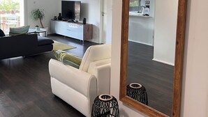 A modern living room with a large mirror, dark wooden flooring, a white sofa, and a television. - Au Coeur du Vignoble, Magnifique vue Avec Terrasse (Westhalten)