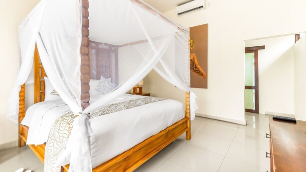 A four-poster canopy bed with a wooden frame and white bedding, a small bedside table, and a wall-mounted air conditioning unit. - Villa Utara - Two Bedroom Villa, Sleeps 4 (Seminyak)