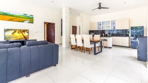 A modern living room with a sofa, dining table, chairs, and a kitchen area with cabinets and appliances. - Villa Utara - Two Bedroom Villa, Sleeps 4 (Seminyak)